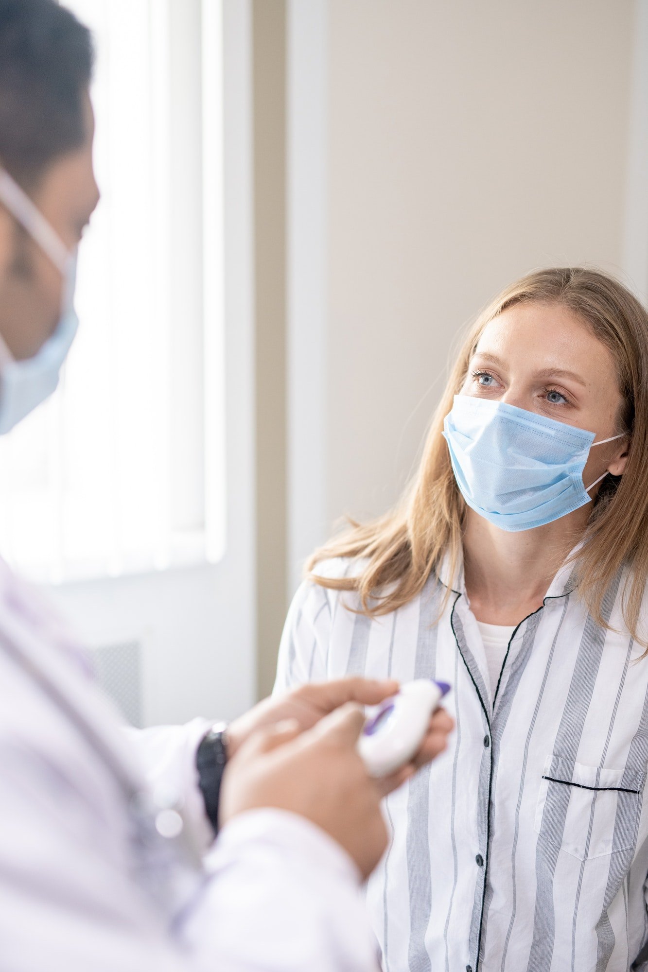 Young female patient in mask looking at her doctor during medical consultation